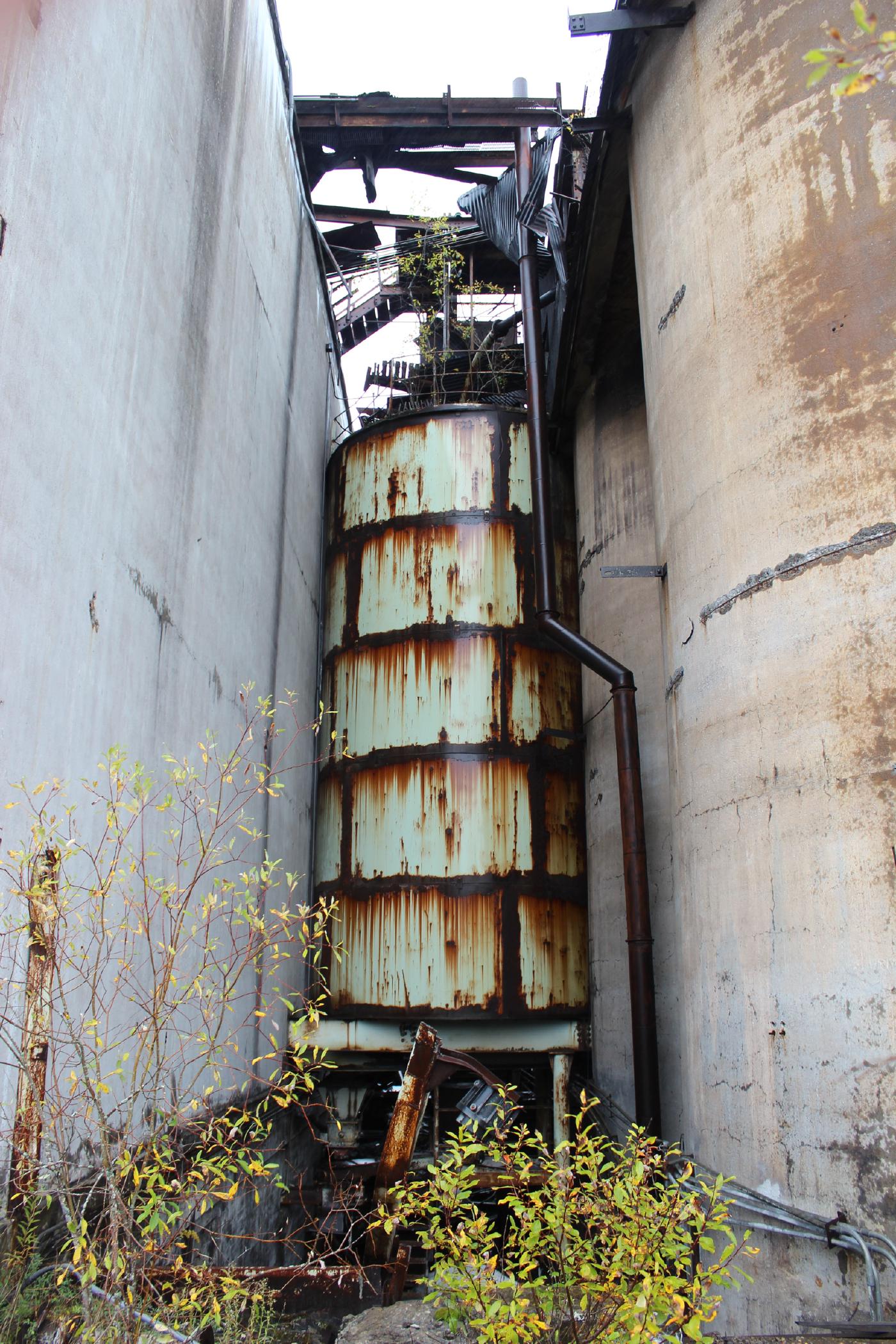 Rusting silo between concrete silos for holding iron ore.